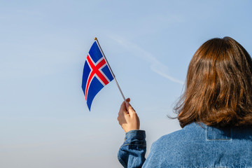 Sticker - Woman hand with Iceland swaying flag on the blue sky. Concept