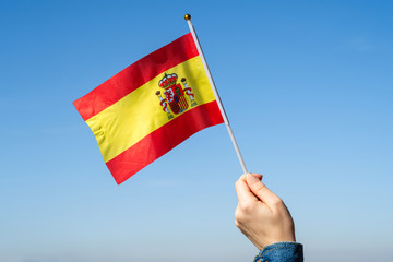 Wall Mural - Woman hand with Spanish swaying flag on the blue sky. Spain. Concept