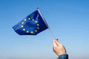 Poster - Woman hand with EU(European) swaying flag on the blue sky. Europe. Concept