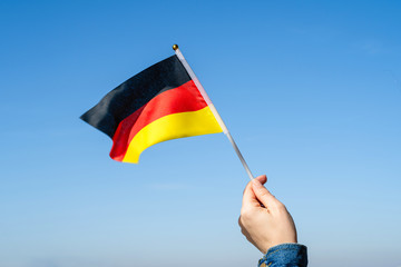 Wall Mural - Woman hand with Germany swaying flag on the blue sky. Concept