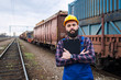 Portrait of railroader foreman holding checklist and controlling cargo dispatch. Freight train with shipping containers in background. Railway transportation.