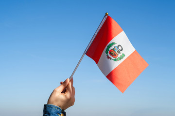 Wall Mural - Woman hand with Peru swaying flag on the blue sky. South America. Concept