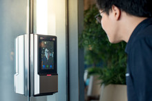 Authentication By Facial Recognition Concept. Biometric Admittance Control Device For Security System. Asian Man Using Face Scanner To Unlock Glass Door In Office Building.