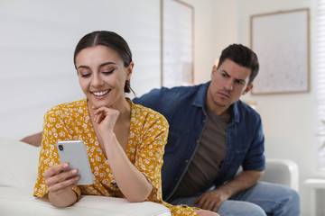 Distrustful man peering into girlfriend's smartphone at home. Jealousy in relationship