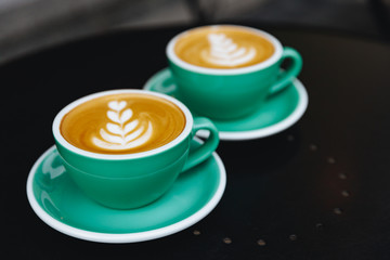 Morning aroma cappuccino with heart pattern in light blue cups with saucers on black table. Break time with coffee. Summer time on comfortable terrace.