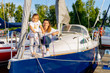© Dawid - Portrait of smiling mother and daughter on prow of sailboat or yacht anchored in marina at bright sunny day. Blurred background with boats and trees