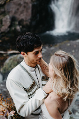 Wall Mural - noise effect, selective focus: incredibly enamored brides hugging, kissing and posing for a photo on the incredible rocky mountains background with a big waterfall