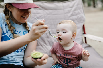 mom feeding her baby daughter an avocado outdoors while camping