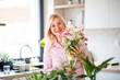 © Halfpoint - Portrait of senior woman arranging flowers in vase indoors at home.
