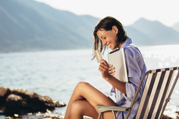 Smiling woman sitting on deck chair by the sea using tablet and credit card on a sunny day