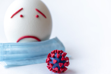 Plasticine model of coronavirus and egg on a white background. Plasticine model of a coronavirus and an Easter egg with a medical mask depicting fear and sadness. Large ostrich egg and coronavirus