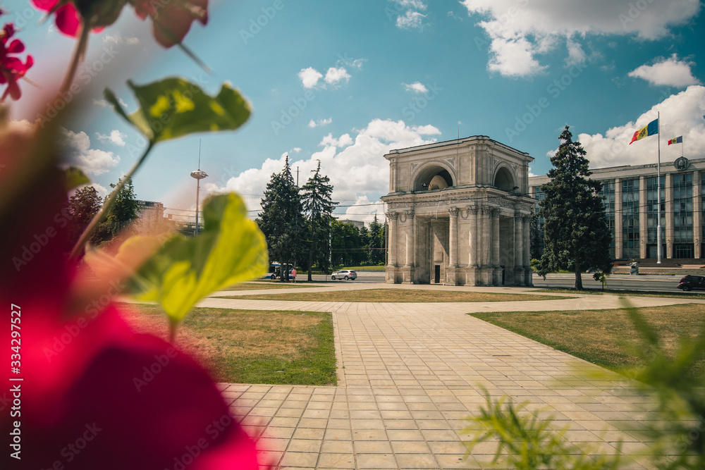 Obraz na płótnie The Triumphal Arch in front of the Government building in Chisinau, Moldova on a warm summer day. Flowers of the park in foreground. w salonie