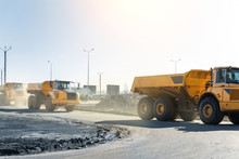 Many Big Articulated Heavy Industrial Yellow Dumper Trucks Driving On New Highway Road Construction Site On Sunny Day With Blue Sky Background. Construction Equipment Machinery Working On Open Pit