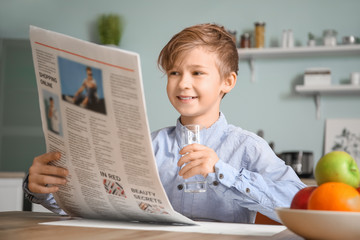 Wall Mural - Cute little boy reading newspaper and drinking water in kitchen