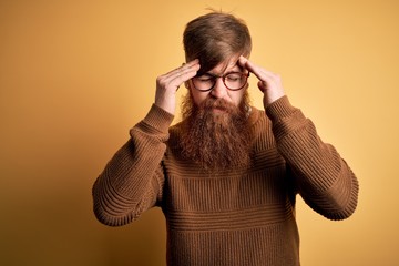 Poster - Handsome Irish redhead man with beard wearing glasses and winter sweater over yellow background with hand on head for pain in head because stress. Suffering migraine.