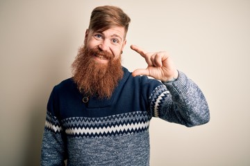 Poster - Handsome Irish redhead man with beard wearing winter sweater over isolated background smiling and confident gesturing with hand doing small size sign with fingers looking and the camera. Measure