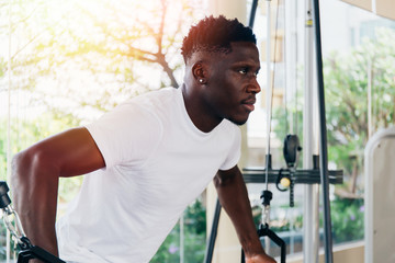 Wall Mural - Muscular African American sportsman doing cable fly with exercise machine standing against window during training in gym.