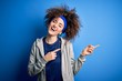 © Krakenimages.com - Young beautiful sportswoman with curly hair and piercing standing wearing sportswear smiling and looking at the camera pointing with two hands and fingers to the side.