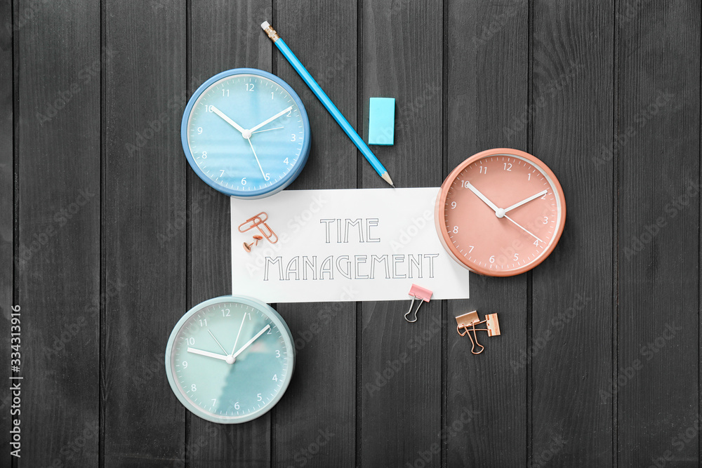Alarm clocks with stationery text TIME MANAGEMENT on dark wooden background