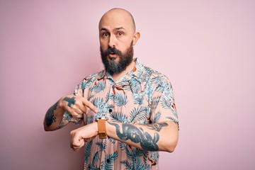 Poster - Handsome bald man with beard and tattoo wearing casual floral shirt over pink background In hurry pointing to watch time, impatience, upset and angry for deadline delay