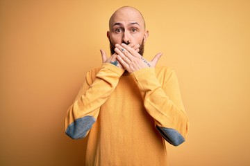 Poster - Handsome bald man with beard wearing casual sweater standing over yellow background shocked covering mouth with hands for mistake. Secret concept.