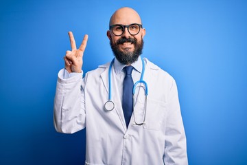 Sticker - Handsome bald doctor man with beard wearing glasses and stethoscope over blue background smiling looking to the camera showing fingers doing victory sign. Number two.