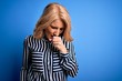 © Krakenimages.com - Middle age beautiful blonde woman wearing casual striped shirt standing over blue background feeling unwell and coughing as symptom for cold or bronchitis. Health care concept.