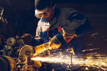 Wall Mural - Locksmith in special clothes and goggles works in production. Metal processing with angle grinder. Sparks in metalworking