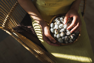 Woman hands holding wooden bowl with quail eggs. Dark background, beautiful natural sun light in kitchen. Easter cooking concept.