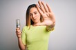 © Krakenimages.com - Young beautiful blonde woman holding led lightbulb over isolated white background with open hand doing stop sign with serious and confident expression, defense gesture