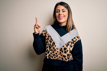 Sticker - Young beautiful woman wearing casual sweatshirt standing over isolated white background pointing finger up with successful idea. Exited and happy. Number one.