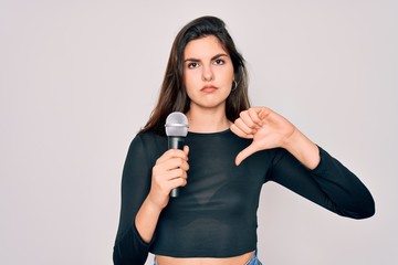 Sticker - Young beautiful singer performer girl singing using music microphone over isolated background with angry face, negative sign showing dislike with thumbs down, rejection concept