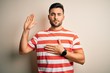 © Krakenimages.com - Young handsome man wearing casual striped t-shirt standing over isolated white background Swearing with hand on chest and open palm, making a loyalty promise oath