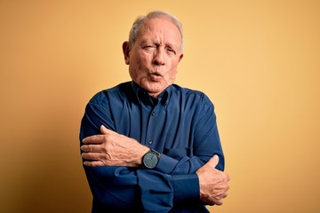 Poster - Grey haired senior man wearing casual blue shirt standing over yellow background shaking and freezing for winter cold with sad and shock expression on face