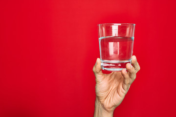 Wall Mural - Beautiful hand of man holding glass of water over isolated red background