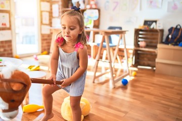 Young beautiful blonde girl kid enjoying play school with toys at kindergarten, smiling happy riding stuffed horse at home