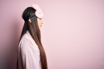 Sticker - Young asian woman wearing pajama and sleep mask over pink isolated background looking to side, relax profile pose with natural face with confident smile.