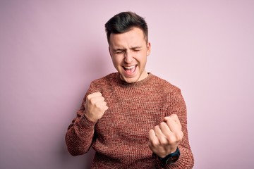 Wall Mural - Young handsome caucasian man wearing casual winter sweater over pink isolated background celebrating surprised and amazed for success with arms raised and eyes closed. Winner concept.