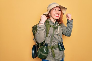 Poster - Young redhead backpacker woman hiking wearing backpack and hat over yellow background excited for success with arms raised and eyes closed celebrating victory smiling. Winner concept.