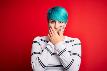 Sticker - Young beautiful woman with blue fashion hair wearing striped sweater over red background shocked covering mouth with hands for mistake. Secret concept.