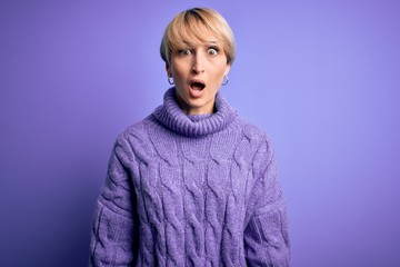 Sticker - Young blonde woman with short hair wearing winter turtleneck sweater over purple background afraid and shocked with surprise and amazed expression, fear and excited face.