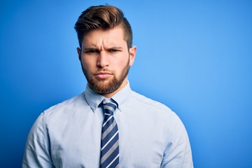 Young blond businessman with beard and blue eyes wearing elegant shirt and tie standing skeptic and nervous, frowning upset because of problem. Negative person.