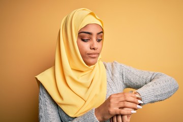 Poster - Young beautiful african american girl wearing muslim hijab over isolated yellow background Checking the time on wrist watch, relaxed and confident