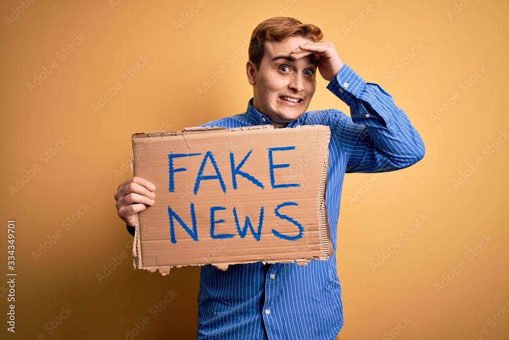 Young handsome redhead man holding banner with fake news message over ...
