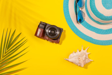 Wall Mural - Top view on beach accessories on yellow background - sunglasses, striped blue hat, camera, sea shell and palm leaf. Concept of the long-awaited vacation at sea and travel. Advertising space