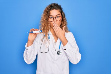 Wall Mural - Young beautiful blonde doctor woman with blue eyes wearing stethoscope holding thermometer cover mouth with hand shocked with shame for mistake, expression of fear, scared in silence, secret concept