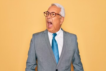 Canvas Print - Middle age senior grey-haired handsome business man wearing glasses over yellow background angry and mad screaming frustrated and furious, shouting with anger. Rage and aggressive concept.