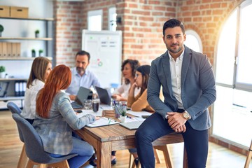 Canvas Print - Group of business workers working together. Young handsome businessman standing smiling happy looking at the camera at the office