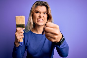 Sticker - Young beautiful blonde painter woman painting using paint bush over purple background annoyed and frustrated shouting with anger, crazy and yelling with raised hand, anger concept