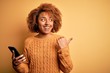 Young African American afro woman with curly hair having conversation using smartphone pointing and showing with thumb up to the side with happy face smiling
